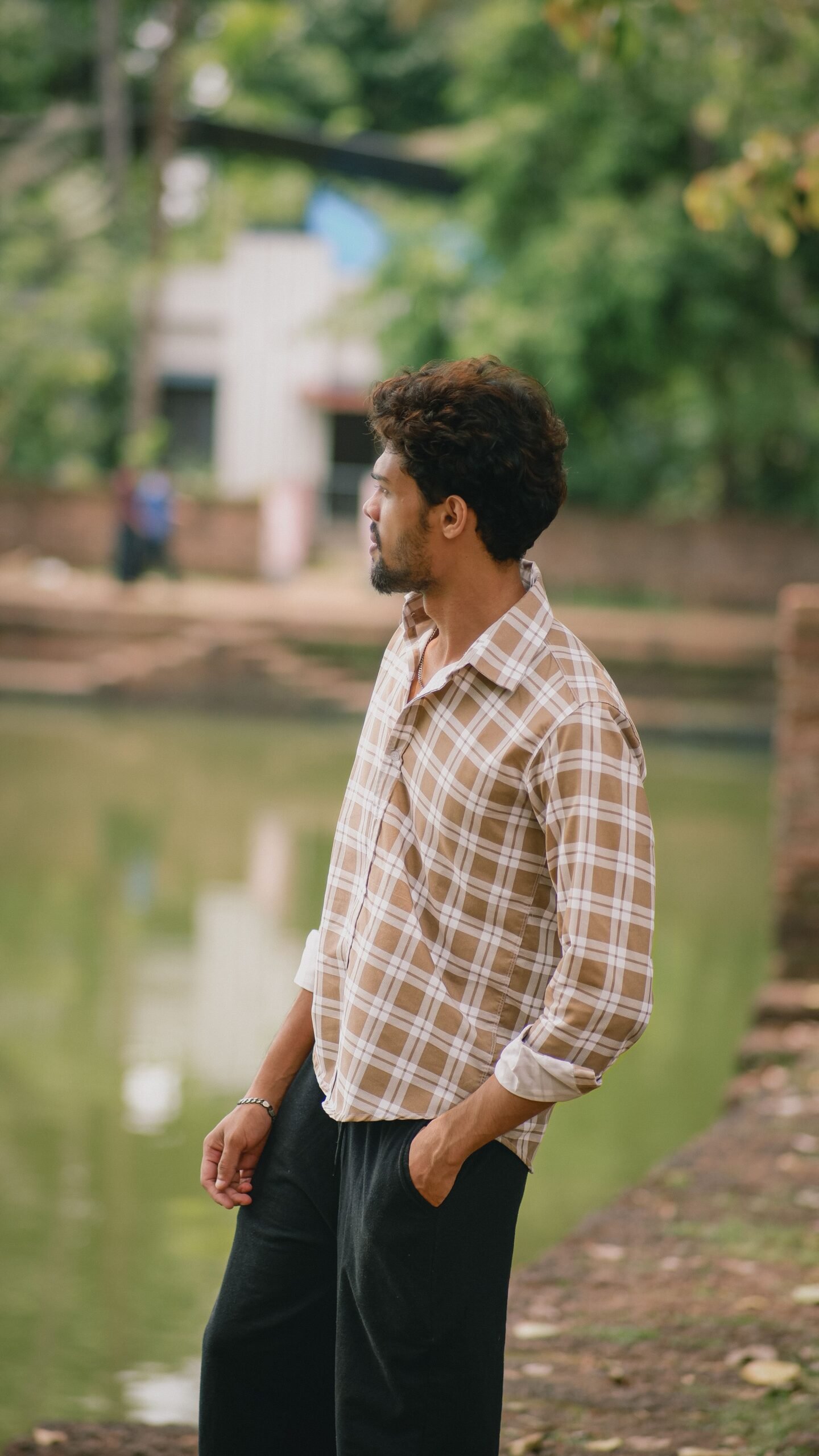 pexels photo 37735681 37735681 Man in plaid shirt gazing thoughtfully across a serene pond, surrounded by lush greenery in a quiet outdoor setting.